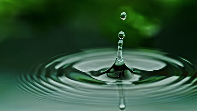 SLOW MOTION Extreme close up droplet splashing, rippling green water surface