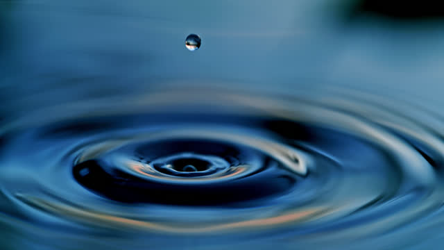 SUPER SLOW MOTION Water droplet falling and rippling blue water surface