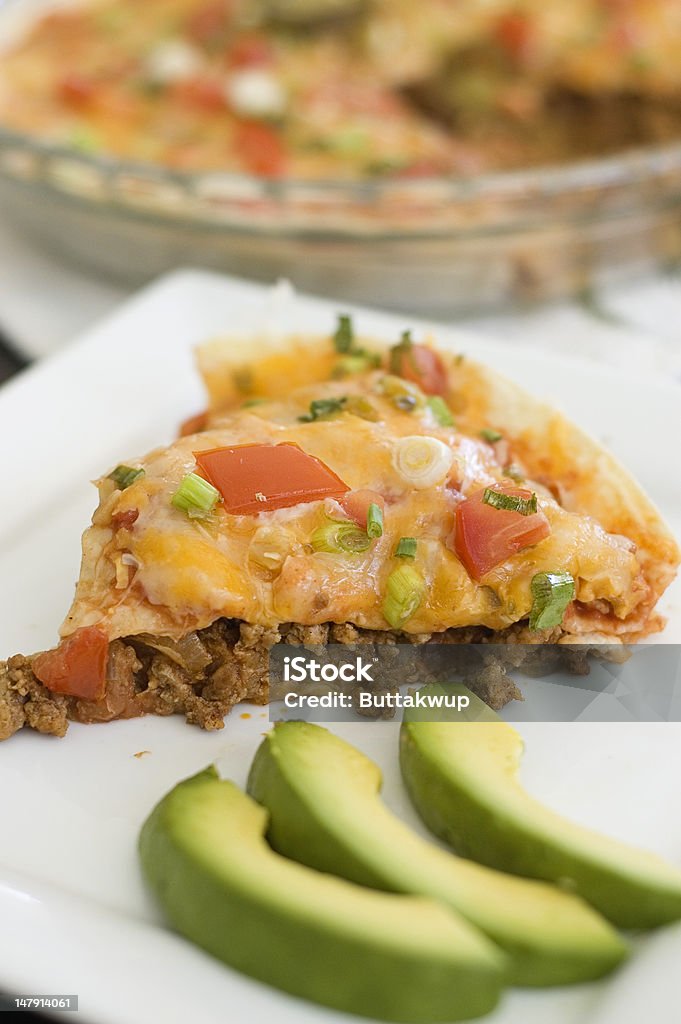 Deep Dish Mexican Pizza Piece of Deep Dish Mexican Pizza served on a white plate and garnished with avocado slices. Pie in Background. Taco Stock Photo