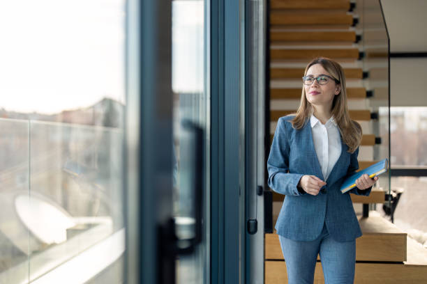 istock Successful businesswoman walking in modern office looking through panoramic window 1479141400