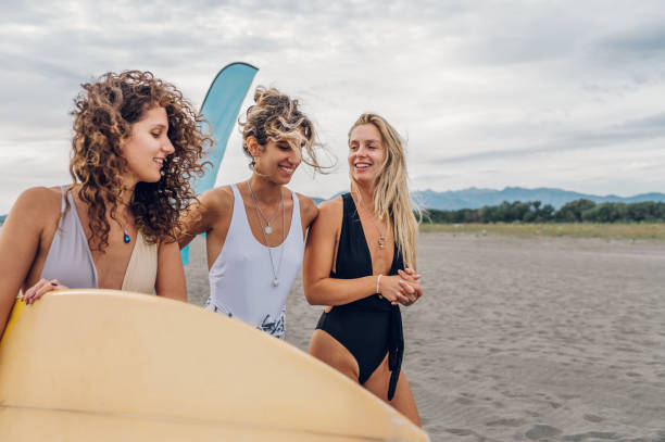 istock Three attractive woman friends walking with surfboard on a beach 1479142490