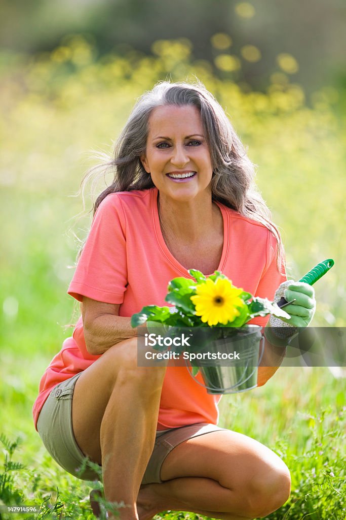 Older Woman Outdoors Holding Flower Pot Close-up shot of beautiful woman in her 50s gardening and smiling for the camera. 50-59 Years Stock Photo