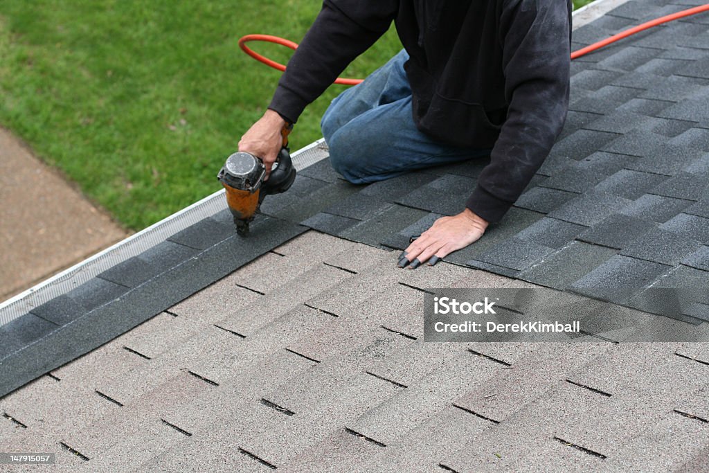 Worker adding shingles to roof Applying a new roof to a home. Repairing Stock Photo