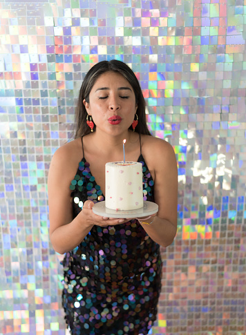 Vertical portrait with high angle view of a woman with elegant dress blowing the candle of birthday cake