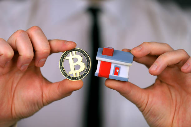 A businessman in a white shirt and black tie holds a bitcoin and miniature house in his hands - fotografia de stock