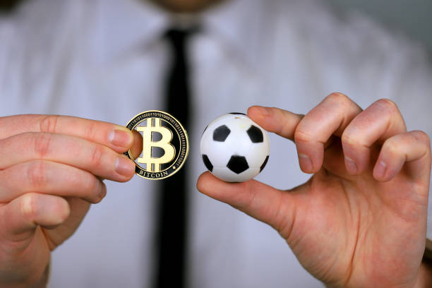 Un uomo d'affari in camicia bianca e cravatta nera che tiene in mano calcio e bitcoin - foto stock
