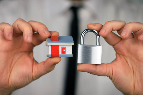 A businessman in a white shirt and black tie holds a silver padlock and miniature house in his hands. Home security stock photo