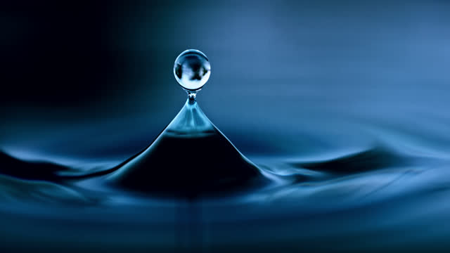 Extreme close up droplet falling and rippling blue water surface