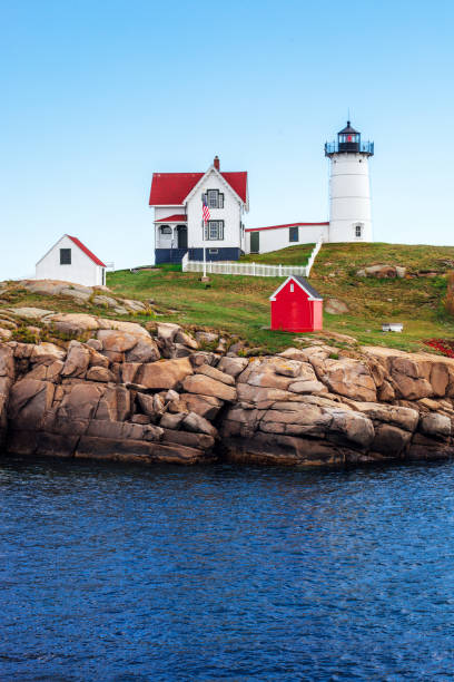 A bench and a thermos of coffee with a view of the sunrise on the coast and a lighthouse in the background. USA. Maine. Nubble Lighthouse