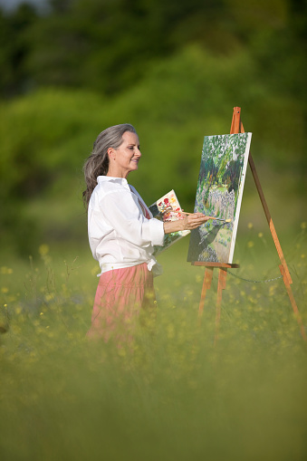 Attractive woman standing in wildflowers painting on canvas.