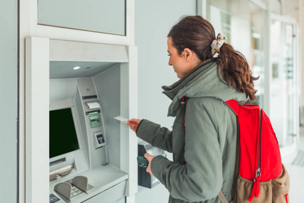 woman uses atm machine to withdraw cash on a busy street - atm human hand bank real people imagens e fotografias de stock