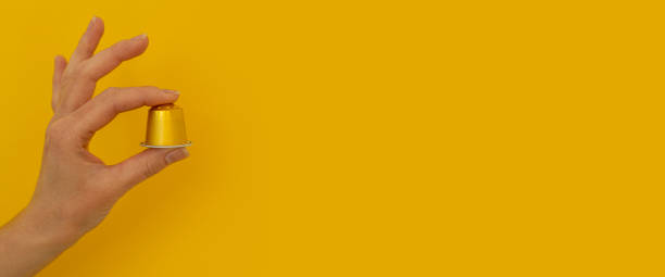 istock Woman's hand holding a coffee capsule on a yellow background. Banner 1479169632