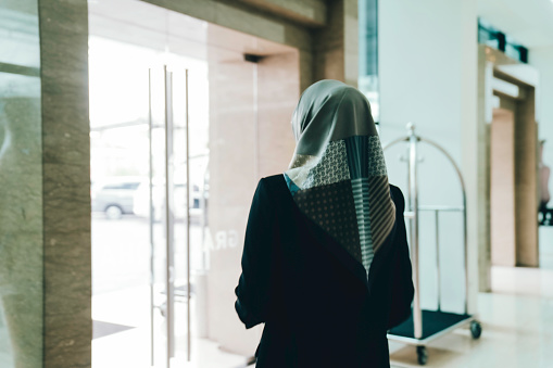 Muslim business  woman pushing the hotel door to leaving   hotel lobby with her suitcase.