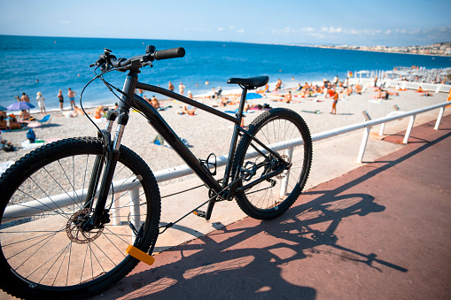 Black bicycle on the sidewalk next to the beach with tourist in summer vacation. Copy space