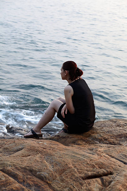 istock Lonely woman sitting on a rock, looking at sea 147917675