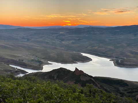 Glowing orange sunrise over East Canyon Reservoir in East Canyon State Park with rolling green hills and unique coastlines