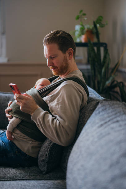 istock A Happy Handsome Ginger Man Using His Mobile Phone While Taking Care Of His Adorable Newborn Child 1479180567