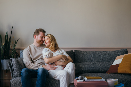 A smiling blonde Caucasian woman holding her cute baby while her ginger husband is hugging her. They are keeping their eyes closed and enjoying being parents. (family concept)