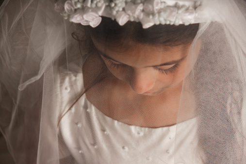 A young girl preparing for her holy communion, photographed with her veil covering her face and looking down