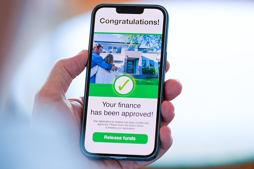 Man looking at a mortgage loan application approval on a mobile phone. There is an image of a house with a happy couple on the phone