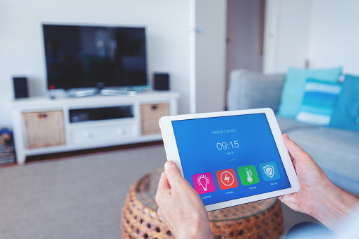 Concept of internet of things and home automation, app on a digital tablet controls household security, energy and surveillance. Man interacts with the touchscreen  in the living room at home.