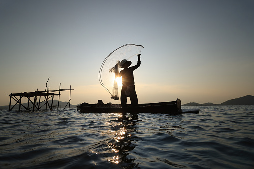 Lifestyle of  fisher man on boat fishing by throwing fishing net, Silhouette  fisherman throwing net hunt fish from reservoir