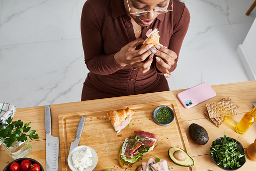 Beautiful young girl preparing sandwiches for social gathering or birthday event, with fresh green salad, ham, cheese, mayo, mustard, tomato, cucumber, pesto, cottage cheese, cream cheese, avocado, Spanish onion with healthy seasoning, herbs and spices, served on a wooden home table, representing a wellbeing and a healthy lifestyle, food indulgence and joy, an image with a copy space