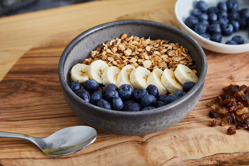 A healthy oatmeal for breakfast, with fresh organic fruit, nuts and grains, at a wooden table in a modern white kitchen, representing a healthy lifestyle, an image with a copy space