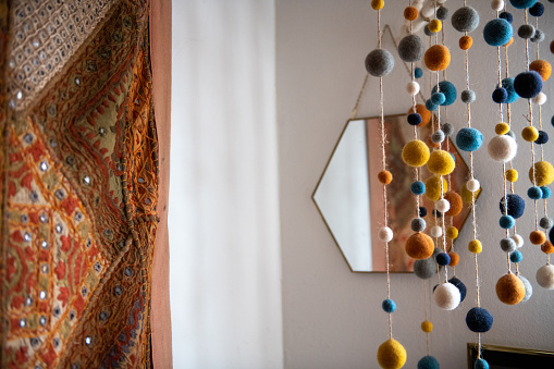 horizontal photo of A beautiful room with colorful pom poms hanging in front of a hexagonal mirror and a rug on the wall