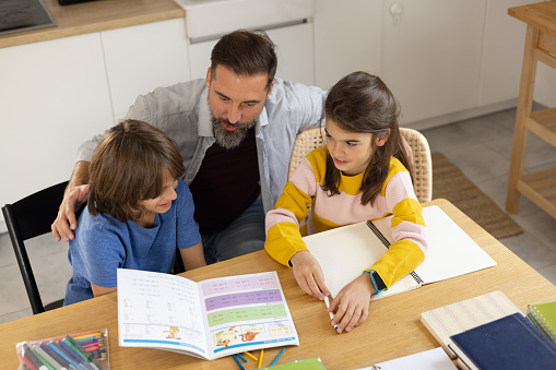 Male caregiver helping two kids with homework at their home