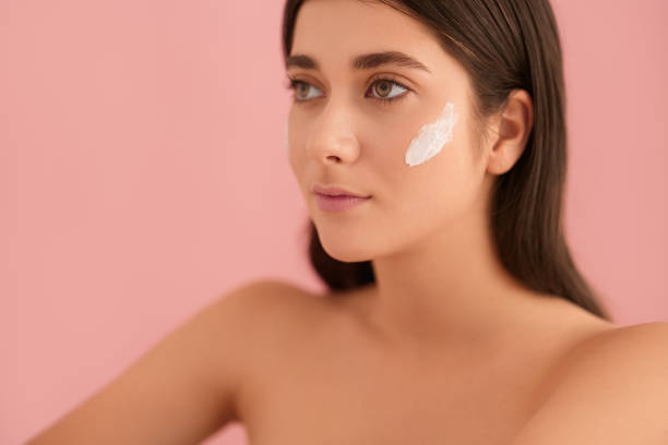 istock Feminine young lady with cream on face looking away in pink studio 1479201594