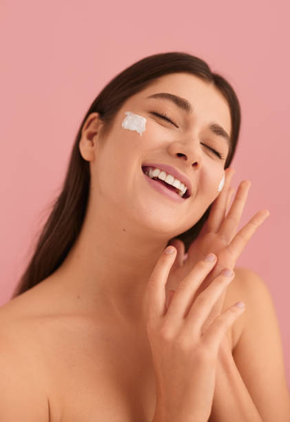 istock Excited young lady applying cream on face and smiling with closed eyes 1479201600