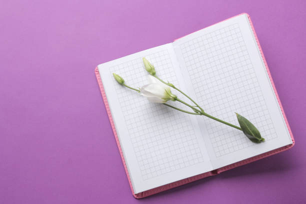 Notepad and beautiful eustoma flowers on a purple background. top view