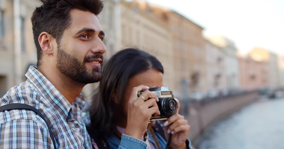 Diverse couple of tourists taking photo on vintage camera in city. Portrait of African-American girlfriend and indian boyfriend travel in european city
