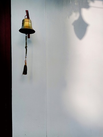 A golden bell was hung in front of the house by the wall. Take photos in the morning when the light hits the wall. This photo was taken in Bangkok, Thailand.