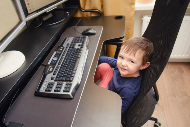 istock Toddler baby works on a computer with a keyboard and mouse. Happy child sits on a computer chair next to the PC monitors. Kid age one year nine months 1479211868