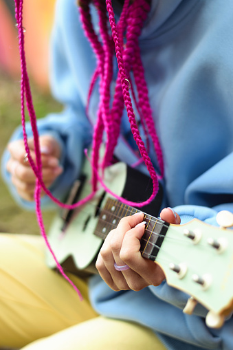 Close-up of Caucasian teenage hipster girl with pink braids playing the ukulele on the street.Summer concept.Generation Z style.