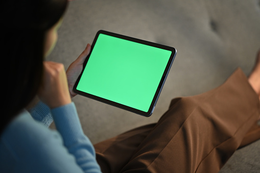 Relaxed young woman using digital tablet on couch at home. Green screen for montage your graphic display.