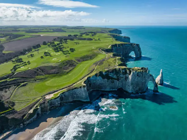 Étretat Coast Normandy, aerial view towards the beach and famous Chalk Cliffs of Etretat - Falaises d’Étretat with Failaise d’Aval and the  L'Aiguille (the Needle) and  Porte d'Aval Natural Arch at the Normandy Alabaster Coast under sunny sky. Drone Point of View. Porte d'Aval , Étretat, Seine-Maritime, Le Havre, Normandy, France, Europe