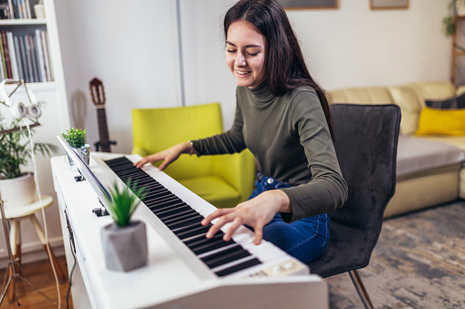 Happy girl is playing piano for her hobby relax time in home living room. Portrait Of Smiling Teenage Girl At Home Playing The Piano