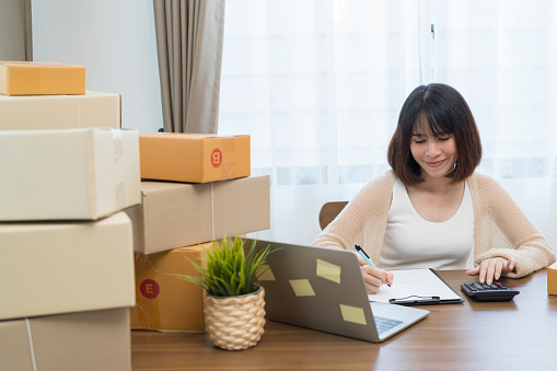Young businessowner excited feel ecstatic reading great on laptop.Pretty and charming young Asian female small online business owner checking her orders on laptop while preparing shipping boxes.