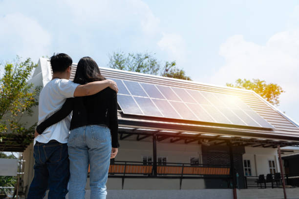 casal feliz se levantando perto de sua casa com painéis solares. energia alternativa, economia de recursos e conceito de estilo de vida sustentável. - solar panel innovation renewable energy alternative energy - fotografias e filmes do acervo