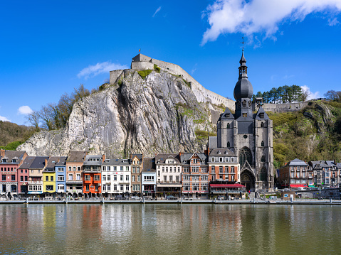 Dinant Cityscape at the waterfront of River Meuse under blue summer sky.  Famous Notre Dame de Dinant Collegial church - Collégiale Notre Dame de Dinant - Church of Our Lady from the 13th-century, old gothic cathedral and huge chalk cliff behind the Town of Dinant. 102 MPixel Hasselblad X2D Cityscape. Dinant, Wallonia, Namur, Belgium, Europe.