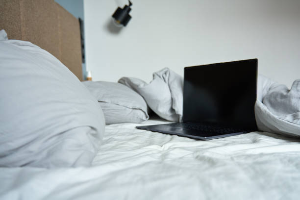 Opened laptop in unmade bed with pillows and crumpled bedsheets at morning. Comfortable workplace for freelancer, work from home