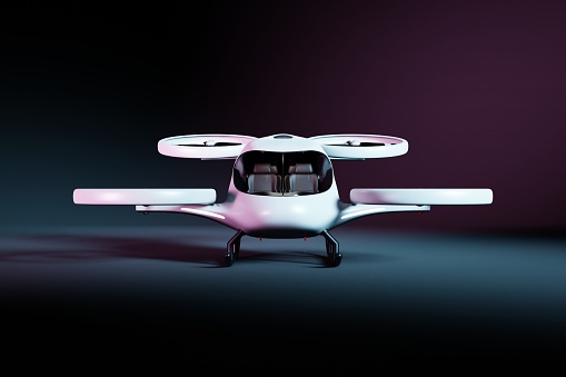 Front view of a white electric vertical take-off and landing aircraft in a dark studio illuminated by light. The background is black. The eVTOL has four propellers. The vehicle is suitable for four passangers.