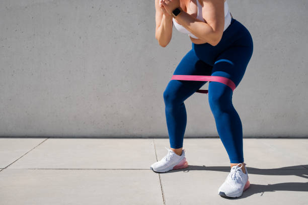 Woman exercising outdoors with resistance band around thighs stock photo