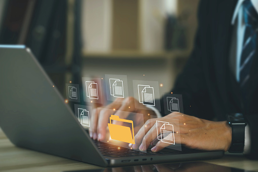 Businessman working on a laptop computer with Document Management System (DMS) Online Document Database and Automation software to archive and efficiently manage information files.Internet Technology.