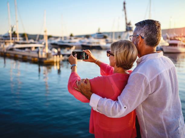 Mature couple in port taking photo with smart phone stock photo