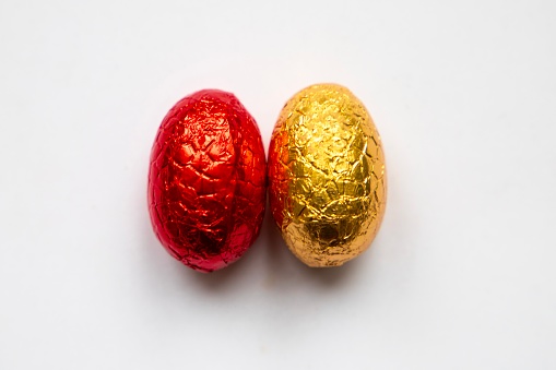 Chocolate Easter eggs wrapped in red and yellow foil on white background
