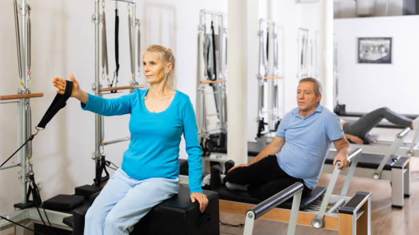 istock Focused elderly man and woman doing stretching exercises while pulling resistance band on Pilates bed machine in studio 1479283969